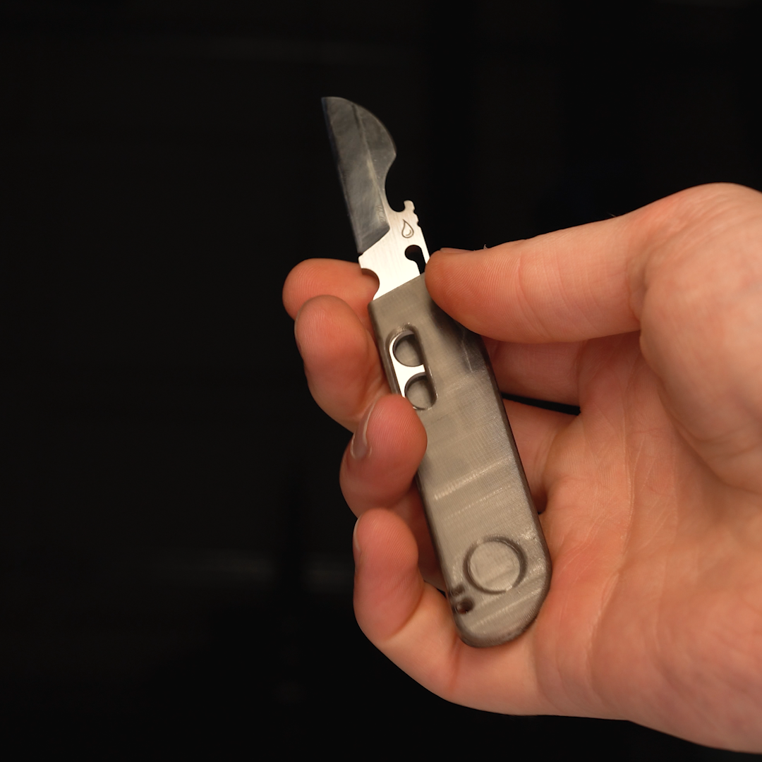 A hand pulls a small fixed blade out of the Sanctum Keeper, a gray sleeve sheath. The Keeper sleeve sheath is flipped 180 degrees and the knife is dropped back in blade first, so the sheath becomes its handle. Invented by Robert van Dyck for Sanctum Brand in October 2026